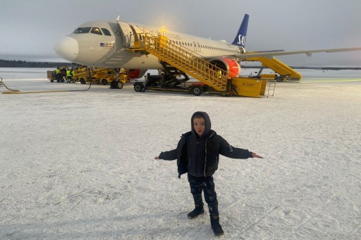Dítě stojící před letadlem na zasněžené přistávací dráze.