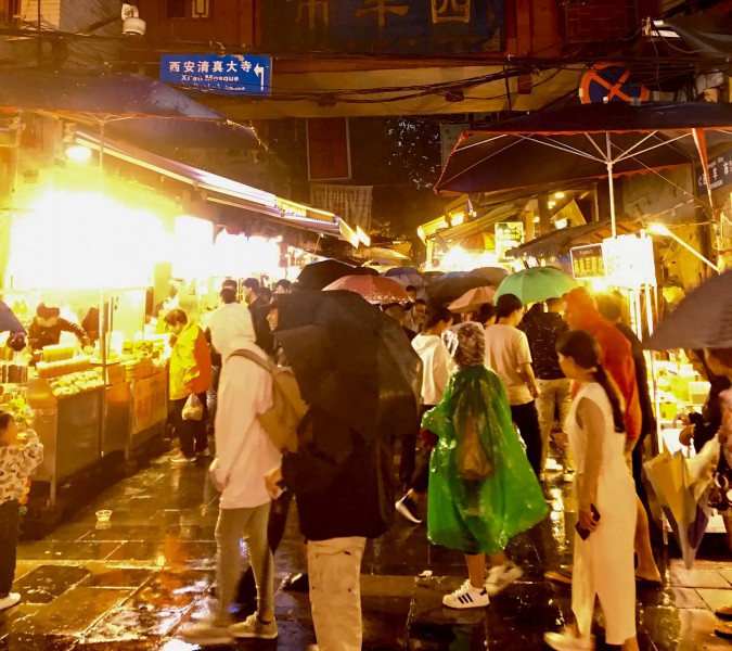  Lidé stojící v dešti a tabulka ukazující směr do mešity v Xianě.