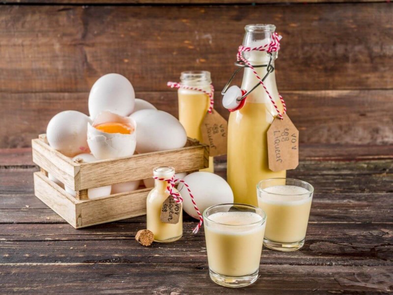 Tradiční vaječný likér Advocaat ve skleněné láhvi a malých skleničkách.