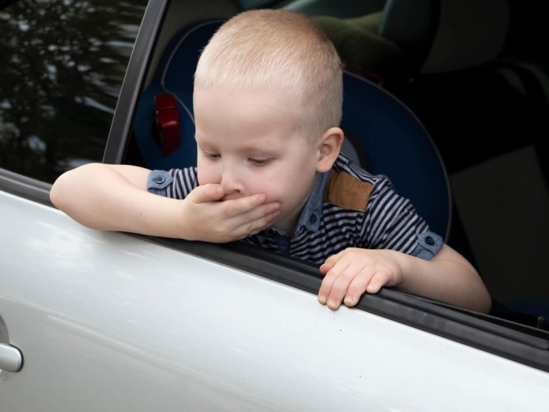 Malé dítě nakloněné z okna auta trpící nevolnostmi z jízdy autem.