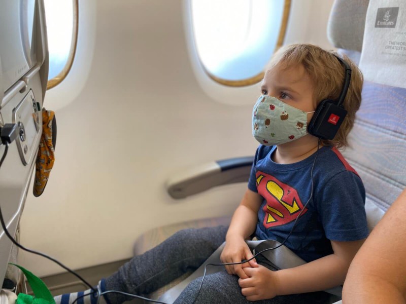 Dítě s rouškou dívající se na pohádky na displeji v letadle.