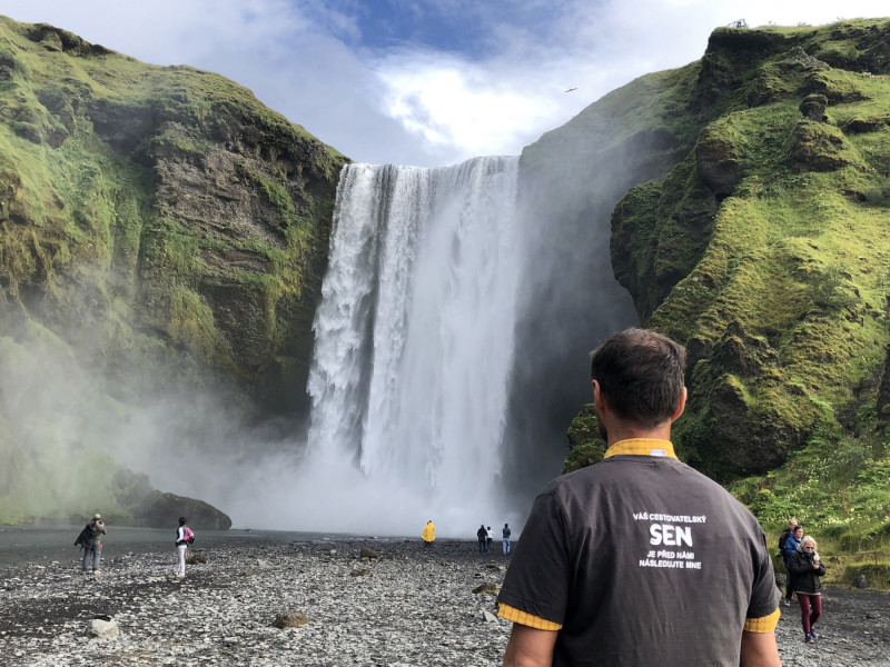 SEN průvodce pozoruje hřmící vodopády Skogafoss na Islandu.