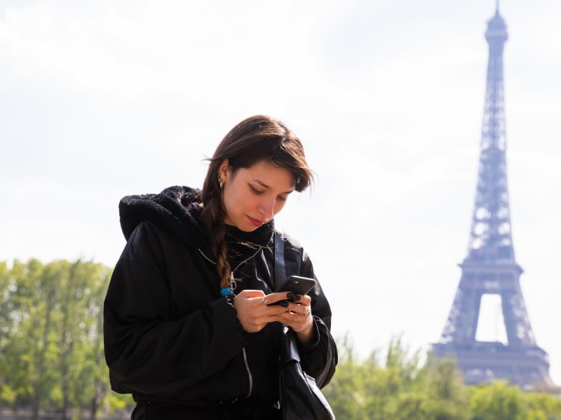 Žena používá mobilní telefon před Eiffelovou věží v Paříži.