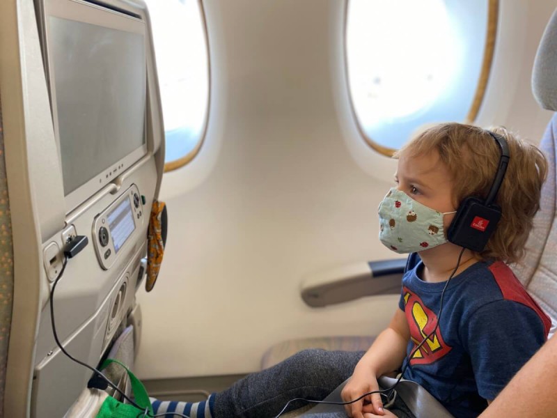 Dítě s rouškou na tváři dívající pohádky na displeji v letadle.