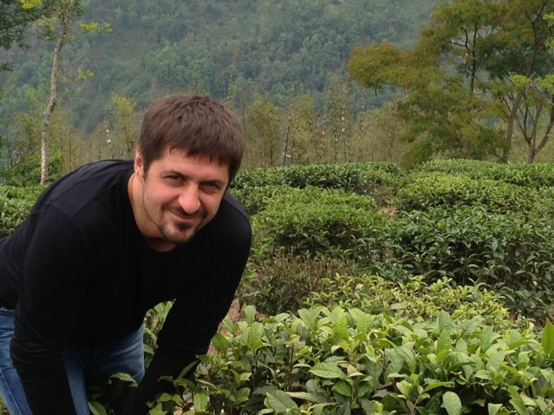 Pavel Fellner na čajové plantáži mezi čajovými keři s horskou krajinou v pozadí.