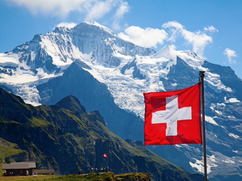 Vlajka Švýcarska se zasněženými horami v pozadí.