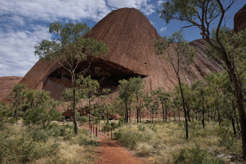 Skalní útvar u Uluru obklopený stromy a stezkou v australském Red Centre.