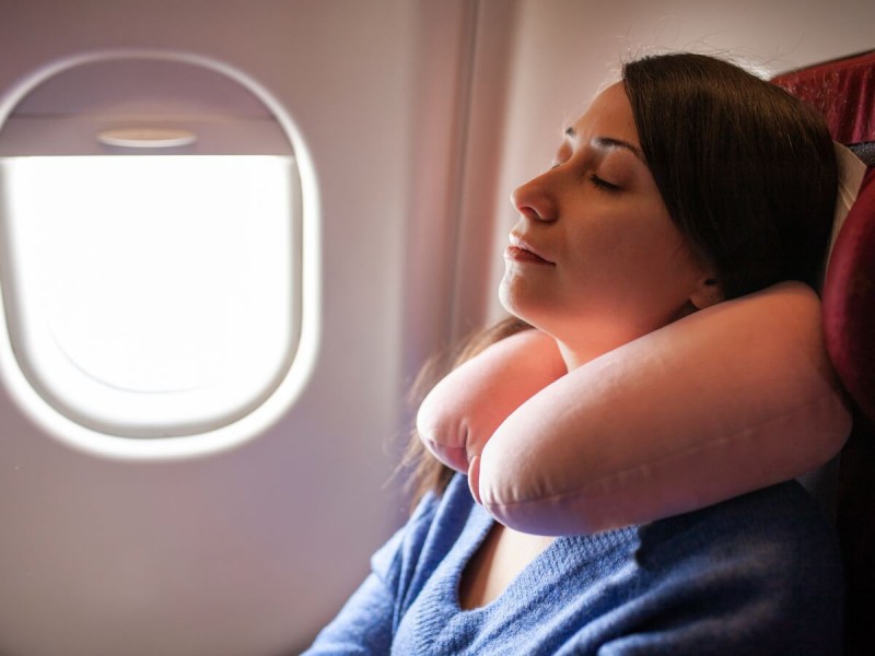 Spící žena s cestovním polštářem kolem krku v letadle.