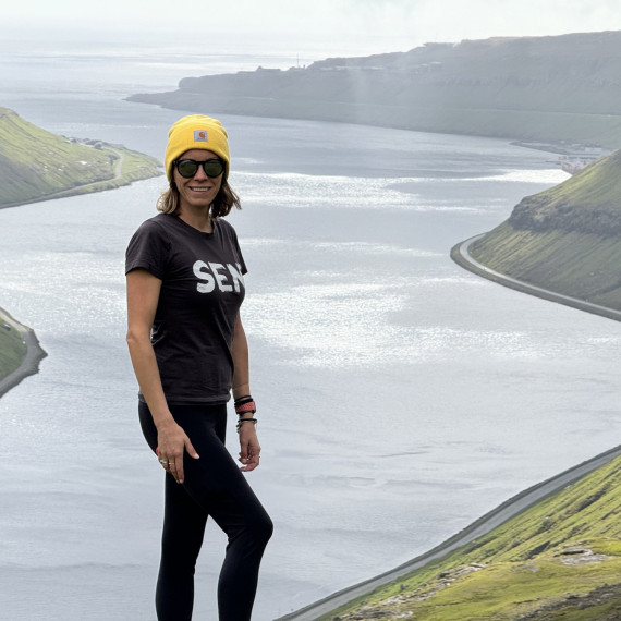 Naše SEN průvodkyně a v pozadí zelené kopce lemující pobřeží Faerských ostrovů.
